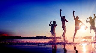 Vier Menschen im seichten Wasser springen glücklich in die Höhe